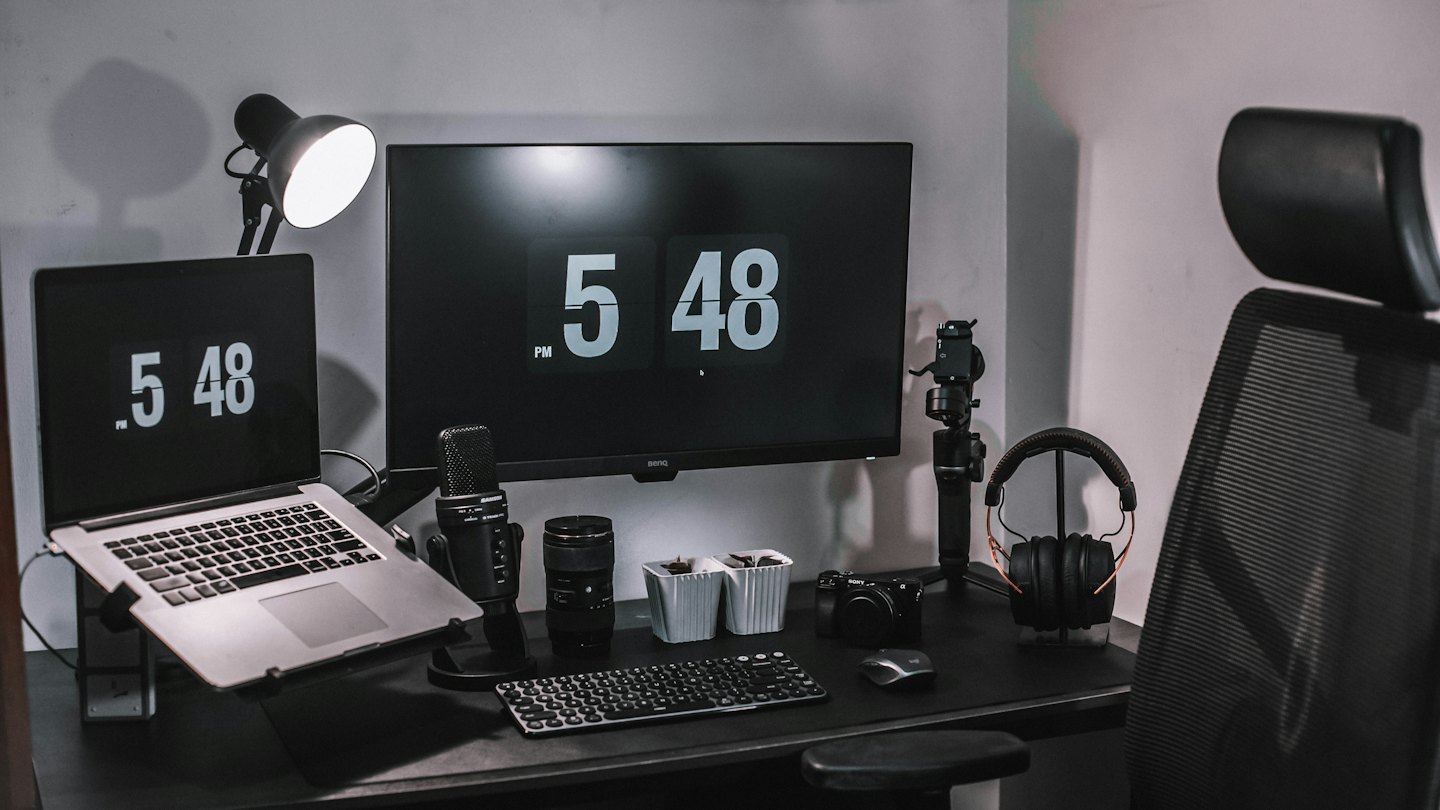 Laptop, monitor y micrófono sobre un escritorio moderno.